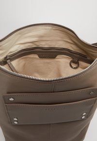 Brun läderhandväska med ett dragkedjeförsett huvudfack, beige foder och en ytterficka med tryckknappar och varumärkeslogotyp.