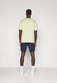 Camiseta corta de manga en verde claro, pantalones cortos azul marino, calcetines blancos y zapatillas, vista desde la parte trasera. Tejido suave, ajuste relajado.