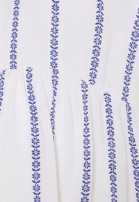 Tessuto bianco con un motivo floreale che presenta fiori blu disposti in linee verticali. La texture appare liscia con leggere arricciature in vita.