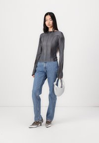 Gray long-sleeve top with panel stitching, paired with light blue jeans. The model holds a silver bag and wears metallic shoes.