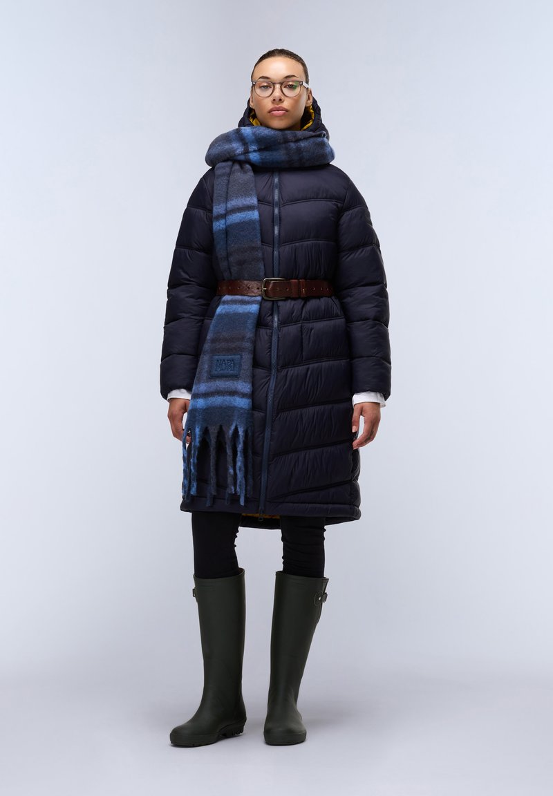 Cappotto imbottito blu navy con cintura, abbinato a una sciarpa a quadretti blu, leggings neri e stivali di gomma verde al ginocchio.