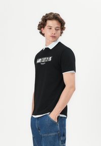 Sort t-shirt med korte ærmer og lyseblå krave samt trykt grafik på fronten. 100% bomuldsstof; afslappet pasform og glat tekstur.