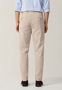 Pantaloni beige slim fit in cotone con due tasche posteriori. Presentano dettagli in metallo dorato e una silhouette pulita e sartoriale.
