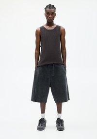 Débardeur noir sans manches en tissu texturé, associé à un short large foncé. Porté avec des baskets noires et des chaussettes blanches. Design simple.