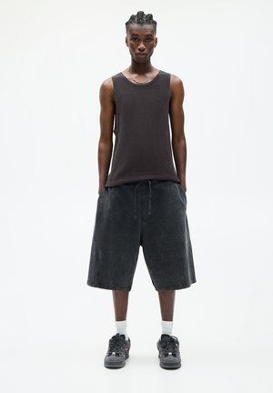 Débardeur noir sans manches en tissu texturé, associé à un short large foncé. Porté avec des baskets noires et des chaussettes blanches. Design simple.