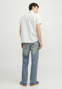 Camisa blanca de manga corta con rayas azules, combinada con jeans de color azul claro y zapatillas azules. La vista trasera muestra un corte casual y un estilo relajado.