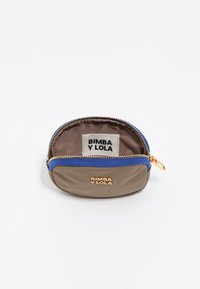 Väike taupe-värvi kott sinise tõmbluku ja kuldse "BIMBA Y LOLA" logoga, avatud, et näidata sisemust ja sildil sama brändinime.