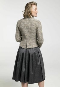 Beige Jacke aus Wollmischung mit strukturierter Oberfläche und taillierter Passform, kombiniert mit einem schwarzen, plissierten Rock mit subtilen Mustern und glänzenden Akzenten.