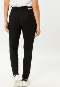 Jeans skinny neri con vita alta, realizzati in un tessuto texture, dotati di tasche posteriori e cucitura piatta sul retro, abbinati a sneakers bianche.