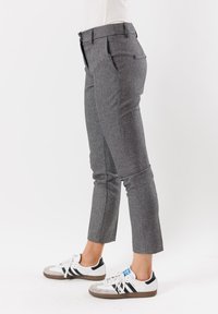 I pantaloni a quadri grigi presentano una vestibilità sartoriale, tasche laterali e un design a gamba corta, abbinati a sneakers bianche con accenti neri.