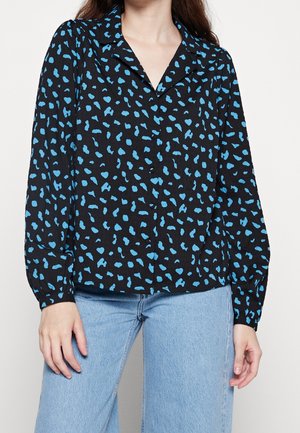 Blusa nera con stampa leopardata blu, maniche lunghe, design con colletto, tessuto leggero, chiusura a bottoni e vestibilità rilassata. Abbinata a jeans azzurri.