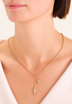 Collar de cadena dorada con dos colgantes: uno con forma de hoja, incrustado con piedras claras, y otro con un diseño elegante de hoja.