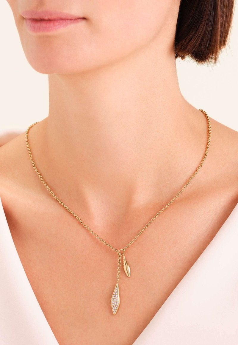 Collier chaîne en or avec deux pendentifs : l'un en forme de feuille, incrusté de pierres claires, et l'autre avec un design élégant de feuille.