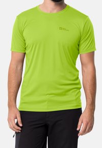 Krátký rukáv, jasně zelené tričko s odváděním vlhkosti vyrobené z hladkého materiálu s malým tištěným logem na hrudi.