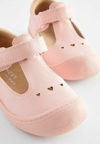 Rosa Leder-Kinderschuhe mit T-Bar-Design, ausgestattet mit herzförmigen Ausschnitten auf der Vorderseite und strukturierten Gummisohlen. Klettverschluss.