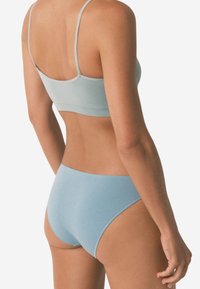 Donna vista da dietro che indossa un reggiseno senza cuciture di un leggero blu e uno slip abbinato a taglio alto su uno sfondo semplice.