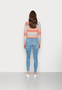 Suéter recortado multicolor con rayas horizontales en durazno, azul y blanco, combinado con jeans ajustados azul claro y zapatillas blancas.