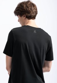 Zwarte katoenen t-shirt met een ontspannen pasvorm. Heeft een ronde halslijn en een klein schaarontwerp op de bovenrug. Soepele textuur.