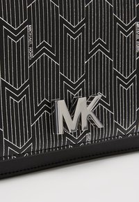 Borsa a tracolla in pelle nera con un motivo geometrico di linee bianche, con un accento in argento del logo MK sulla parte anteriore.