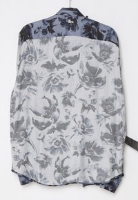 Chemise à manches longues à motif floral en tons gris avec empiècement floral foncé contrastant, suspendue sur un fond blanc.