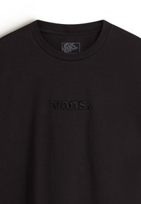 Camiseta de algodón negra con cuello redondo y un logo bordado "vans." en el mismo color en el pecho. Textura suave.
