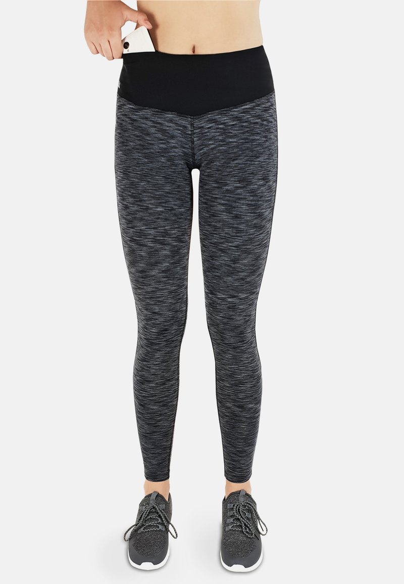 Schwarze und graue Sportleggings mit hohem Bund, strukturiertem Muster und einer Tasche am Bund; kombiniert mit grauen Sportschuhen.