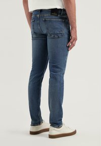 Vékony, koptatott kék farmernadr�ág hátsó zsebekkel és derékra varrt címkével, fehér tornacipővel párosítva.