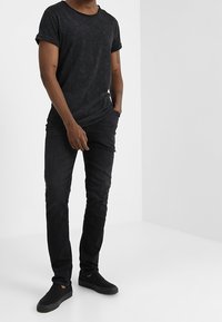 Camiseta negra de manga corta con un acabado suave y texturizado, combinada con jeans ajustados negros y zapatos negros de slip-on. Diseño minimalista.