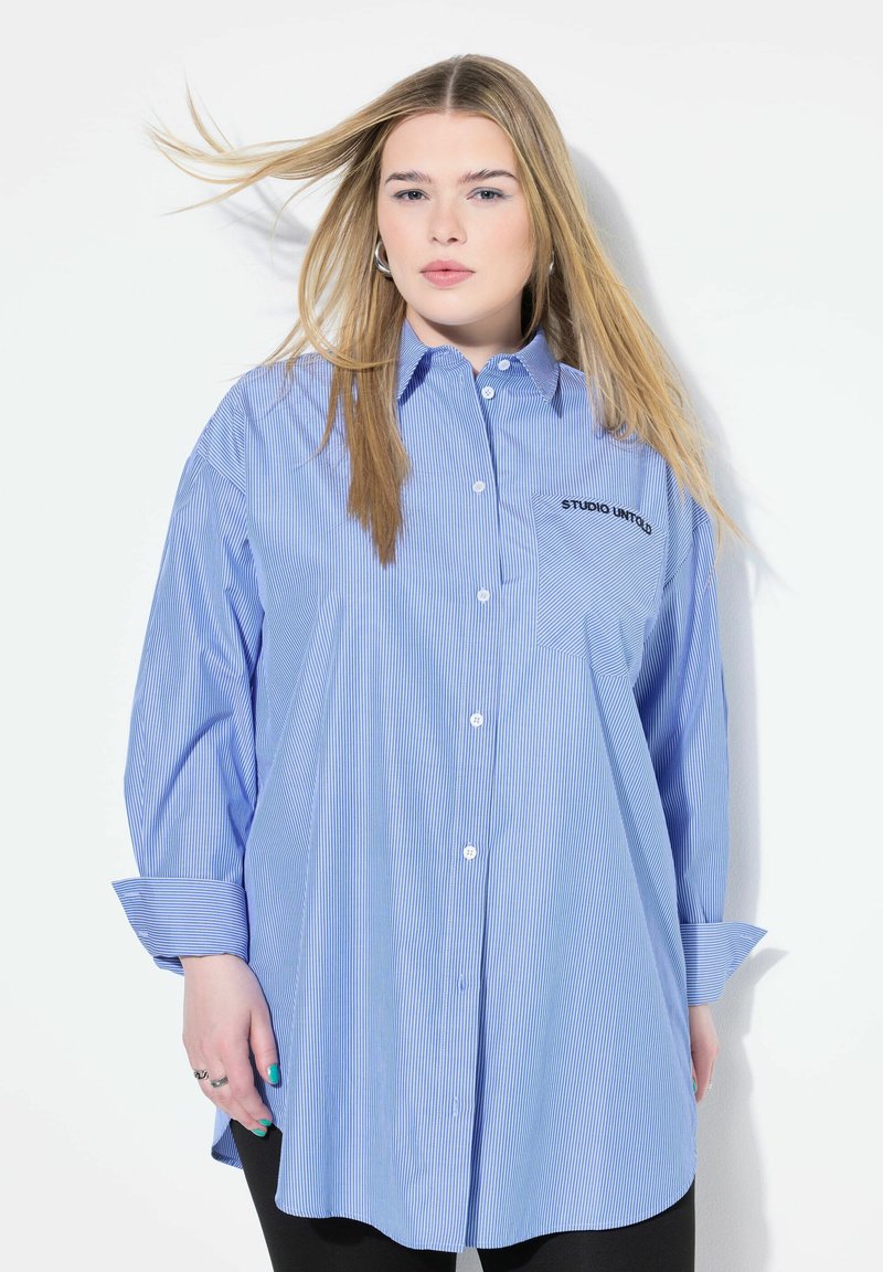 Camicia a righe blue e bianco con bottoni, maniche lunghe, taschino con la scritta "STUDIO UNITED" e vestibilità comoda. Tessuto morbido.