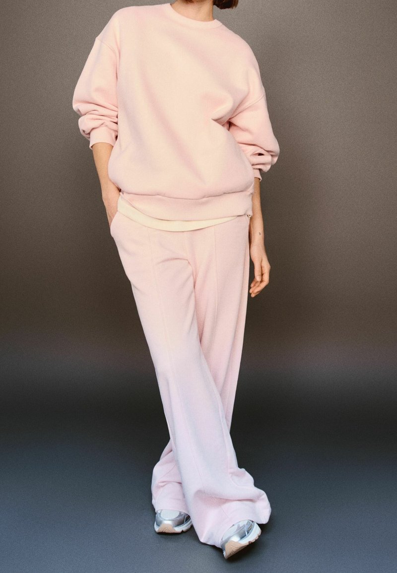 Sweatshirt rose clair et pantalon de survêtement assorti en tissu doux. La silhouette est décontractée, avec un col rond et des poignets côtelés, associés à des baskets argentées.