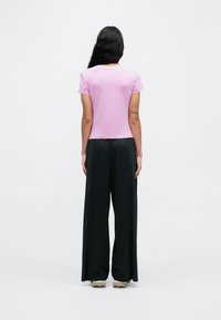 Różowy t-shirt z krótkim rękawem w zestawieniu z czarnymi, szerokimi spodniami o luźnym kroju i gładkiej fakturze. T-shirt posiada okrągły dekolt.