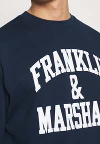 Felpa blu navy con grandi scritte bianche "FRANKLY & MARSHALL" in caratteri grassetto. Realizzata in morbido cotone con collo rotondo.