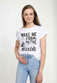Hvid t-shirt med korte ærmer, der har et sort grafisk print af en kvinde og teksten "VÆK MIG TIL WEEKENDEN." Blå jeans.