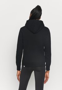 Schwarzer Kapuzenpullover mit lockerer Passform, gerippten Bündchen und Saum. Glatte Textur mit dezentem Markenetikett am unteren Saum.