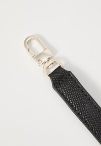 Černý texturovaný kožený pás s zlatým kovovým zapínáním, který obsahuje kulaté kroužkové spojení. Design je elegantní a praktický.