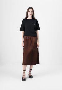 T-shirt nero a maniche corte con dettagli ricamati, abbinato a una gonna marrone al ginocchio e ballerine nere con lacci alla caviglia.