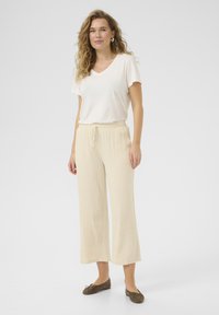 Beige Weitbeinige Hosen mit einem elastischen Kordelzugbund, kombiniert mit einem weißen V-Ausschnitt-T-Shirt. Glatte Stofftextur, lässige Passform und braune Ballerinas.