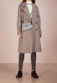 Cappotto doppiopetto a motif checked, in tonalità grigio e marrone; abbinato a una borsa grigia e scarpe platform scure, con pantaloni grigi.