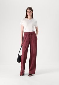 White short-sleeve t-shirt paired with high-waisted maroon wide-leg trousers featuring a drawstring. Model holds a black handbag.