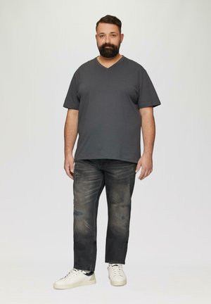 T-shirt gris foncé à col en V, jean foncé usé et baskets blanches. Design simple et coupe décontractée, avec des signes visibles d'usure sur le jean.