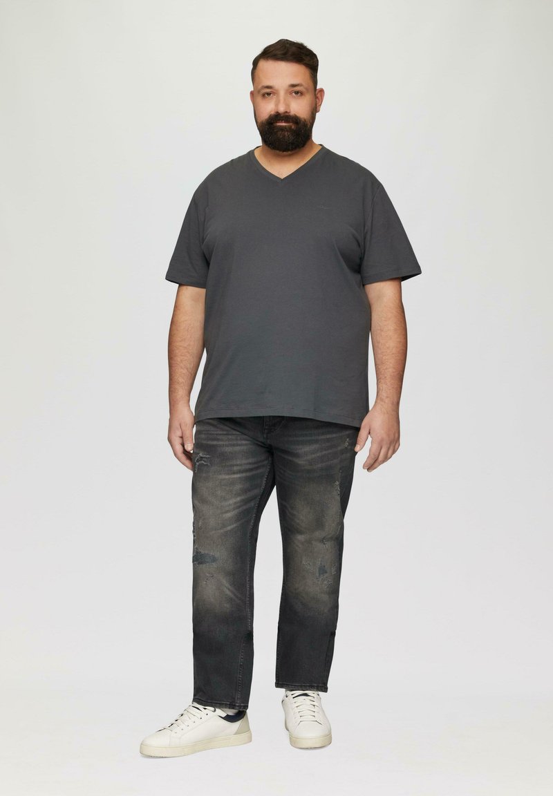 T-shirt gris foncé à col en V, jean foncé usé et baskets blanches. Design simple et coupe décontractée, avec des signes visibles d'usure sur le jean.