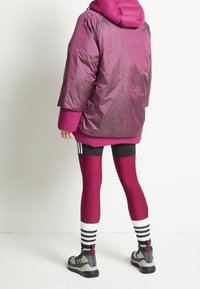 Vadderad vinröd jacka med huva, bärs över svarta shorts och åtsittande vinröda leggings. Svartvita randiga strumpor och grå sportskor.