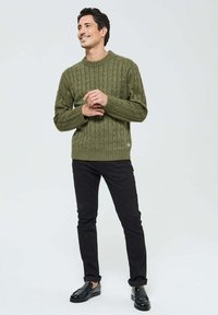 Pull en maille vert olive avec motif en câble et bordures côtelées, associé à un pantalon noir et des mocassins noirs. Design simple, tissu texturé.
