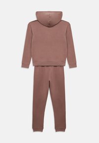 Φόρμα με κουκούλα σε απόχρωση σκονισμένο ροζ, κατασκευασμένη από μαλακό ύφασμα. Διαθέτει μακριά μανίκια και παντελόνι με στενή γραμμή, με ριμπ μανσέτες και μέση.