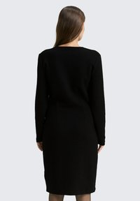 Schwarzes langärmliges Kleid aus strukturiertem Stoff, mit taillierter Silhouette und knielangem Schnitt, in einem einfachen, minimalistischen Design.