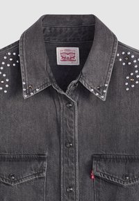 Chemise en denim noir avec boutons-pression, deux poches avant et clous métalliques le long des épaules. Étiquette Levi's au col.