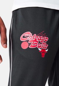 Schwarze Sporthosen mit einem roten "Chicago Bulls"-Logo, das eine Basketballgrafik und einen Stierkopf zeigt, akzentuiert mit weißen Seitenstreifen.