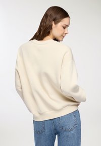 Sweatshirt oversize color crema con scollatura rotonda e spalle scese. Tessuto morbido e testurizzato con polsini a costine. Indossato con jeans a vita alta.