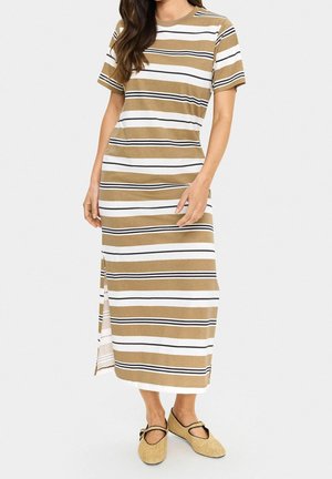 Mujer vistiendo un vestido con mangas cortas, largo hasta el tobillo, a rayas en tonos beige, blanco y negro con zapatos planos beige con tiras negras.