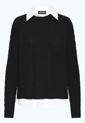 Mustmust tekstuuriga sviiter ümmarguse kaelusega ja pikkade varrukatega, mille alla on kihtide kaupa pandud valge kraega särk. Omab nöörknit-mustrit.